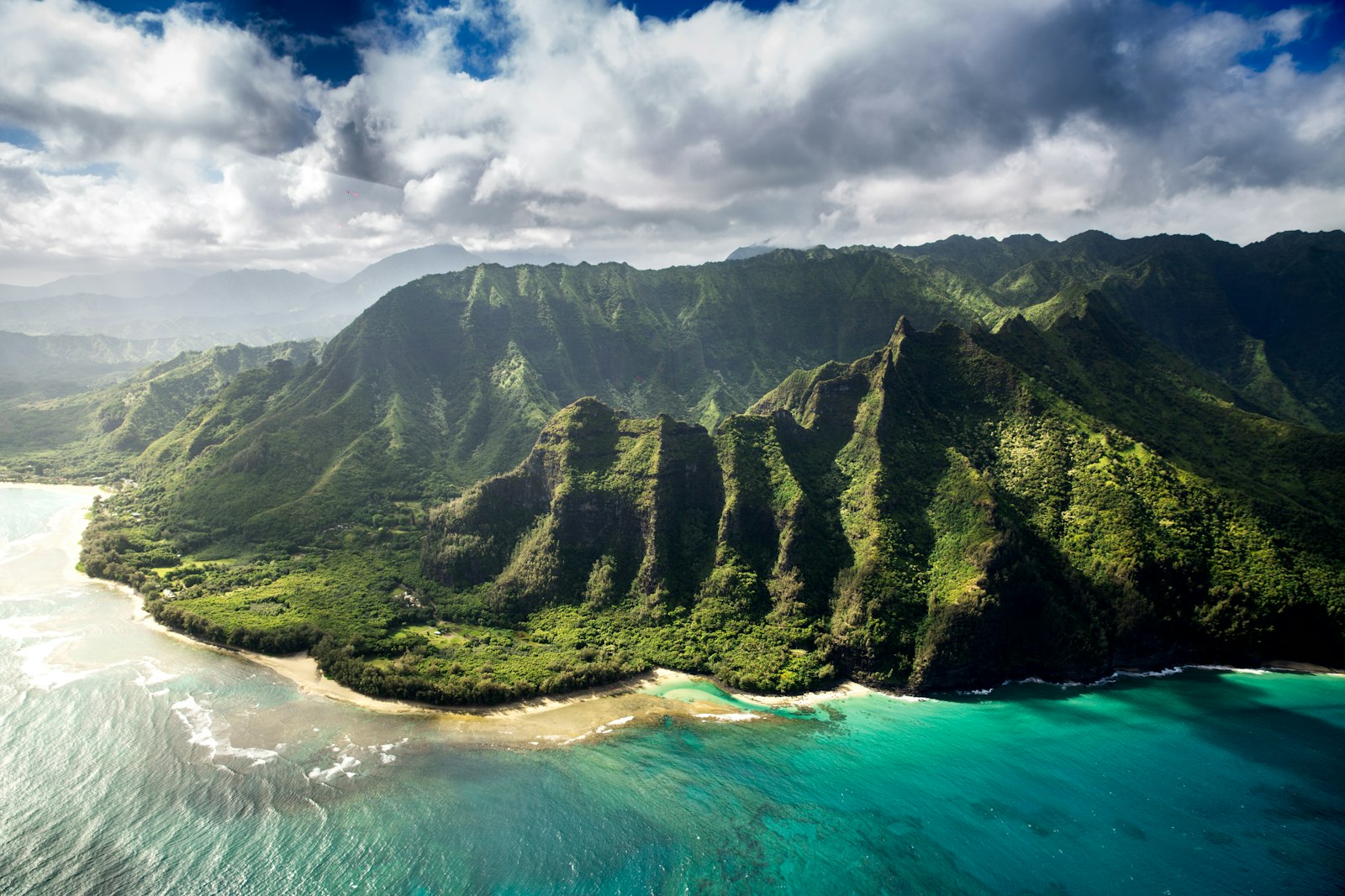 Aerial view of green mountains meeting turquoise water in Hawaii